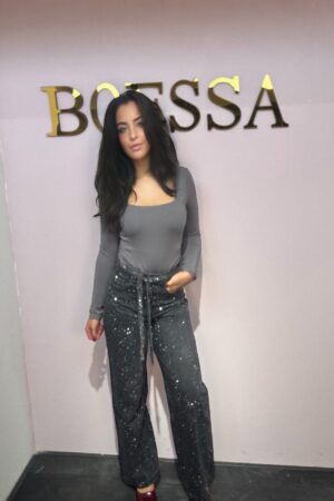 Model draagt een grijze glitterbroek met strasstenen, hoge taille, rechte pijpen – feestelijke damesbroek one size tot maat 42.