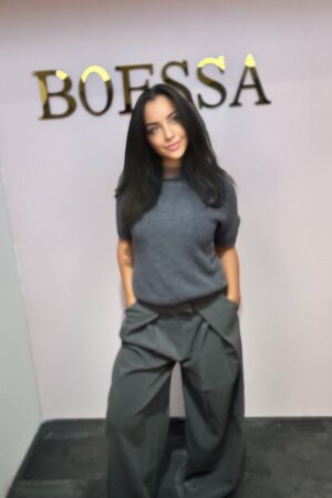 Model draagt de Ambika Wide Leg Pantalon in chocoladebruin, met hoge taille, diepe plooien en extra wijde pijpen.