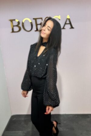 Model draagt een pailletten jumpsuit met lange mouwen, open rug en aangesloten pantalon, perfect voor feestelijke gelegenheden.